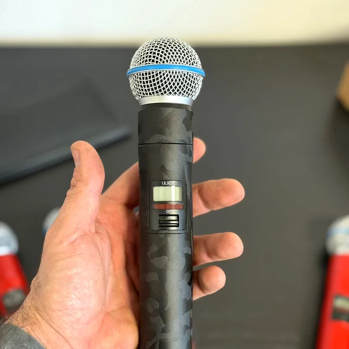 Hand holding a wireless Shure ULXD2 microphone wrapped in a black camouflage print