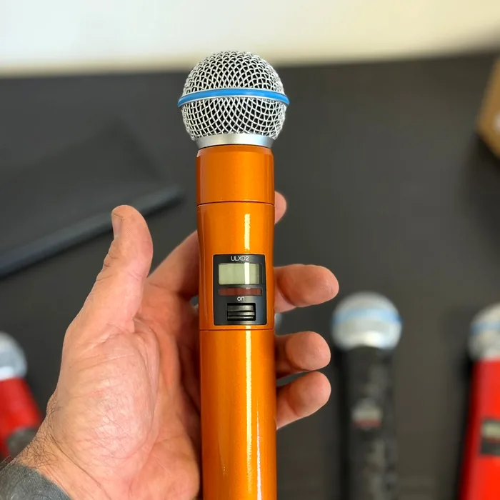 Hand holding a wireless Shure microphone wrapped in metallic orange