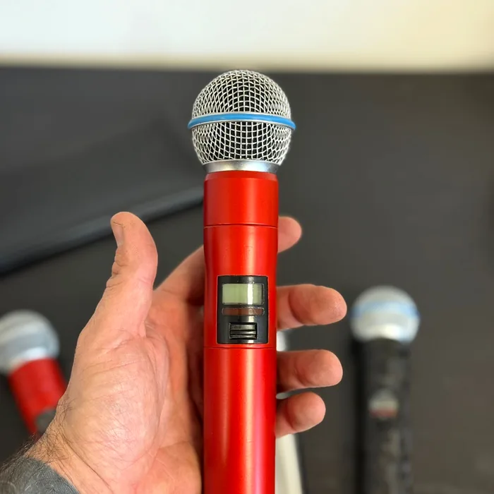 Hand holding a wireless Shure microphone wrapped in satin red