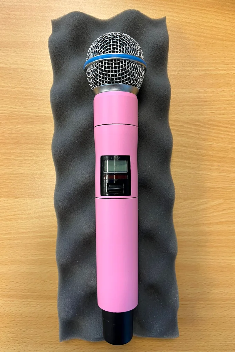 The same wireless Shure microphone in matt pink, seen from above on grey foam