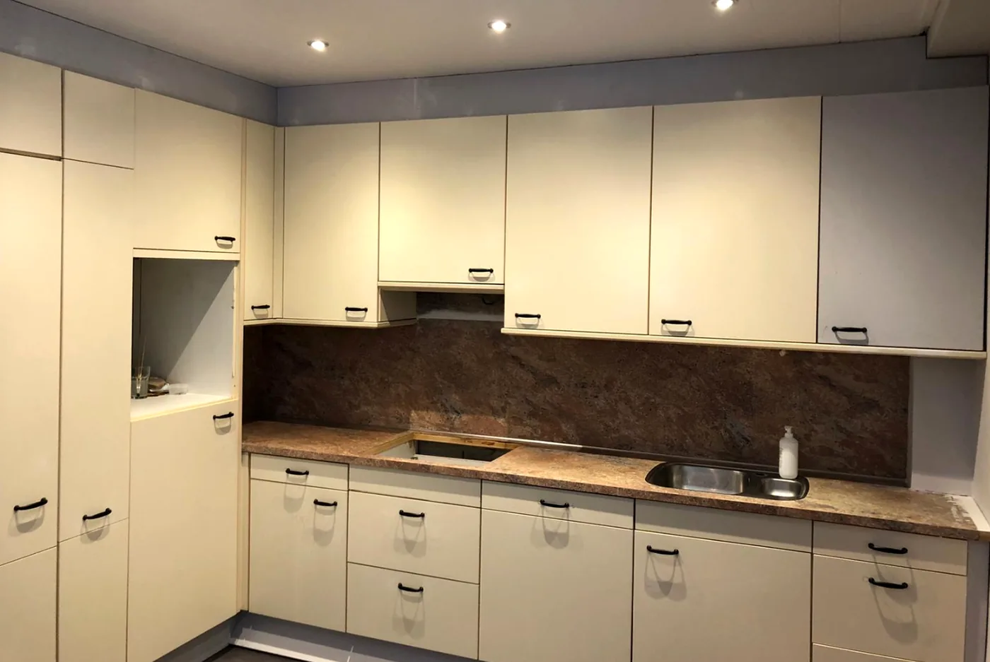 Before: the same kitchen in cream with a reddish-brown granite worktop and splashback
