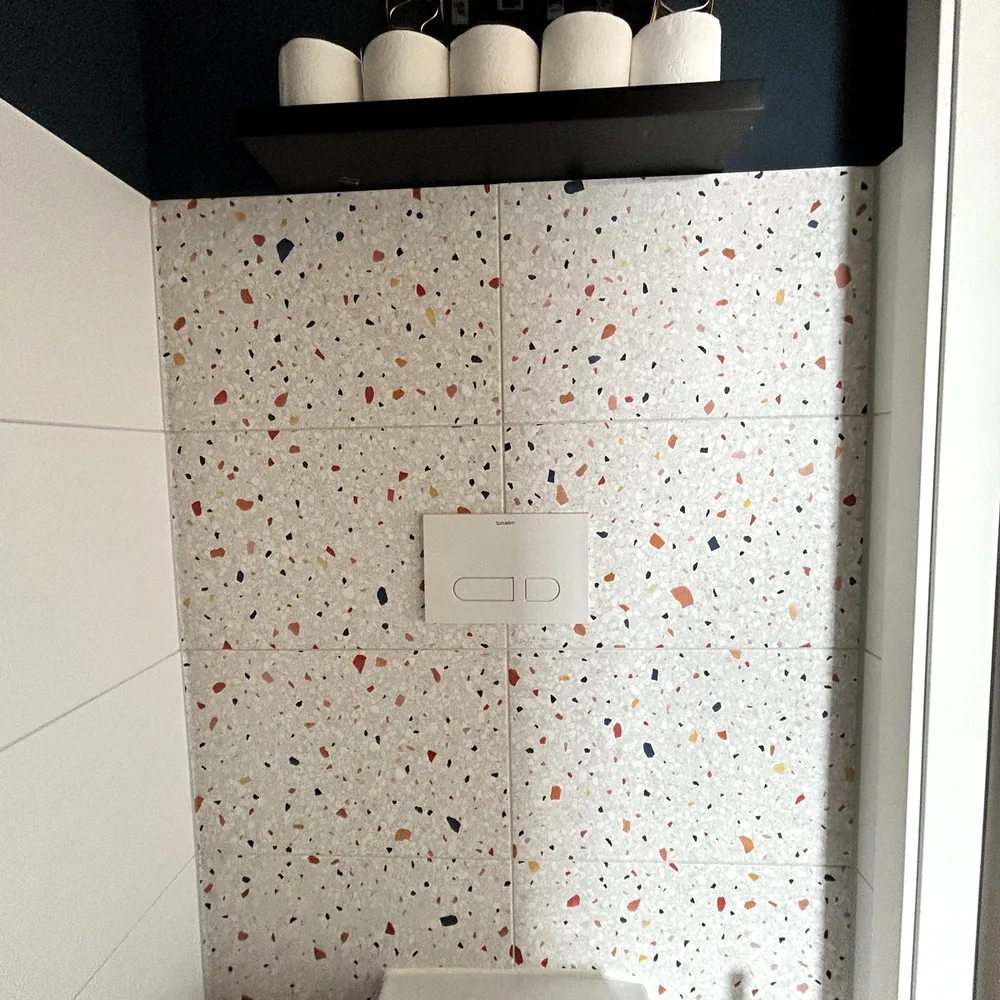 Washroom with the tiled wall wrapped in a terrazzo look, under a black shelf