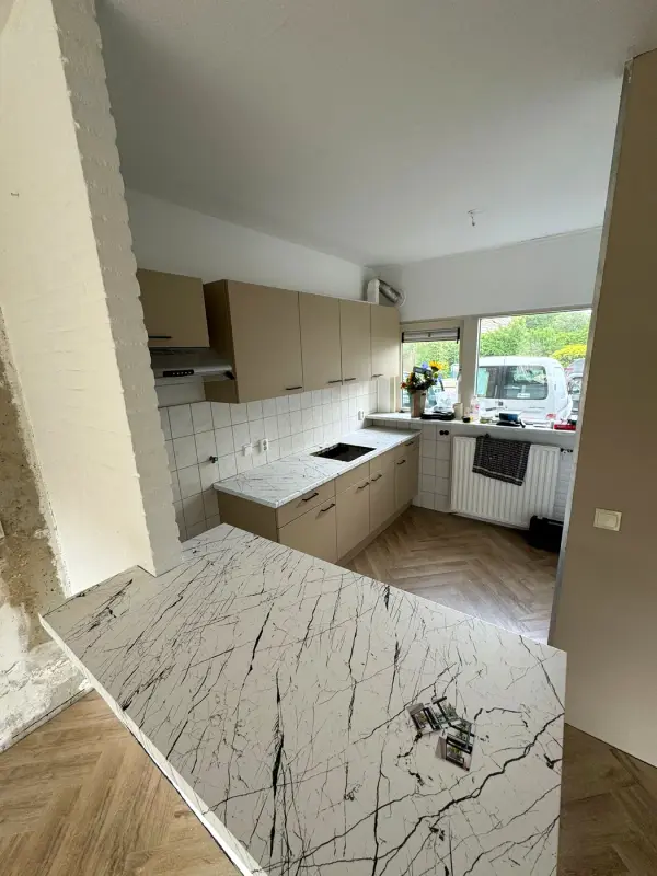 Overview of the taupe kitchen with the peninsula in a white marble look