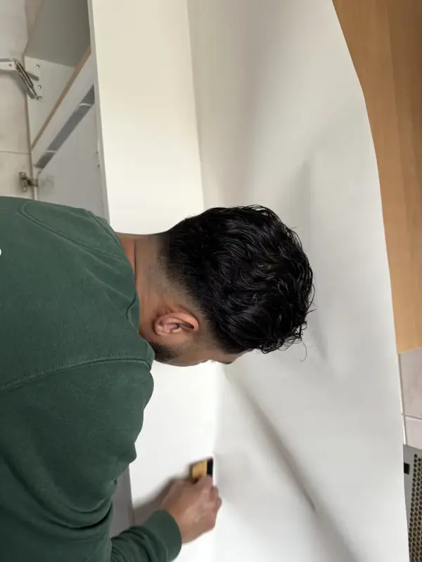 A fitter smooths white film along the edge of a wall