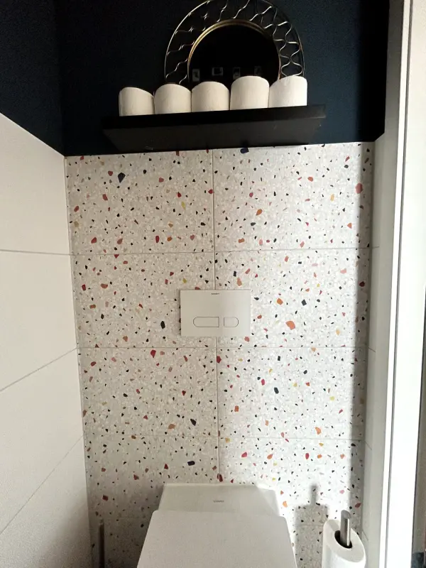After: washroom with a tiled wall in a terrazzo look and a wall-hung toilet